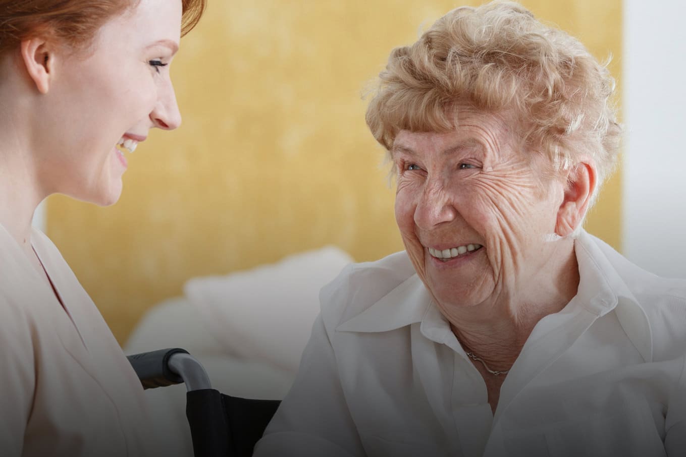 Rothaarige Pflegerin im Gespräch mit einer Seniorin im Pflegeheim